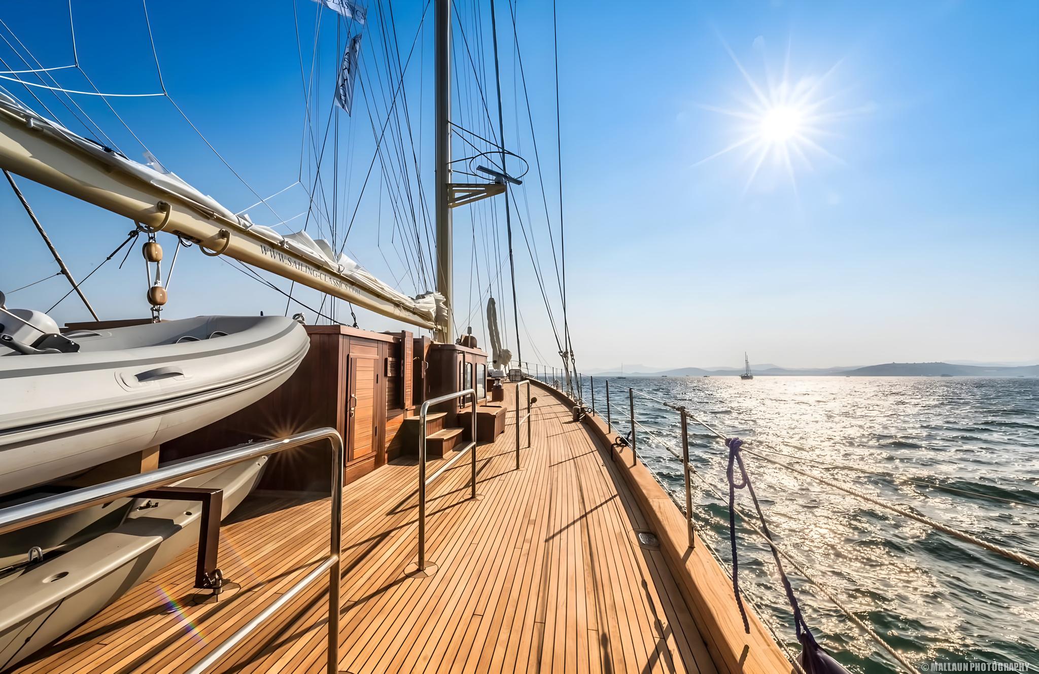 gulet side deck with teak planking, white tender, mast rigging and open sea view