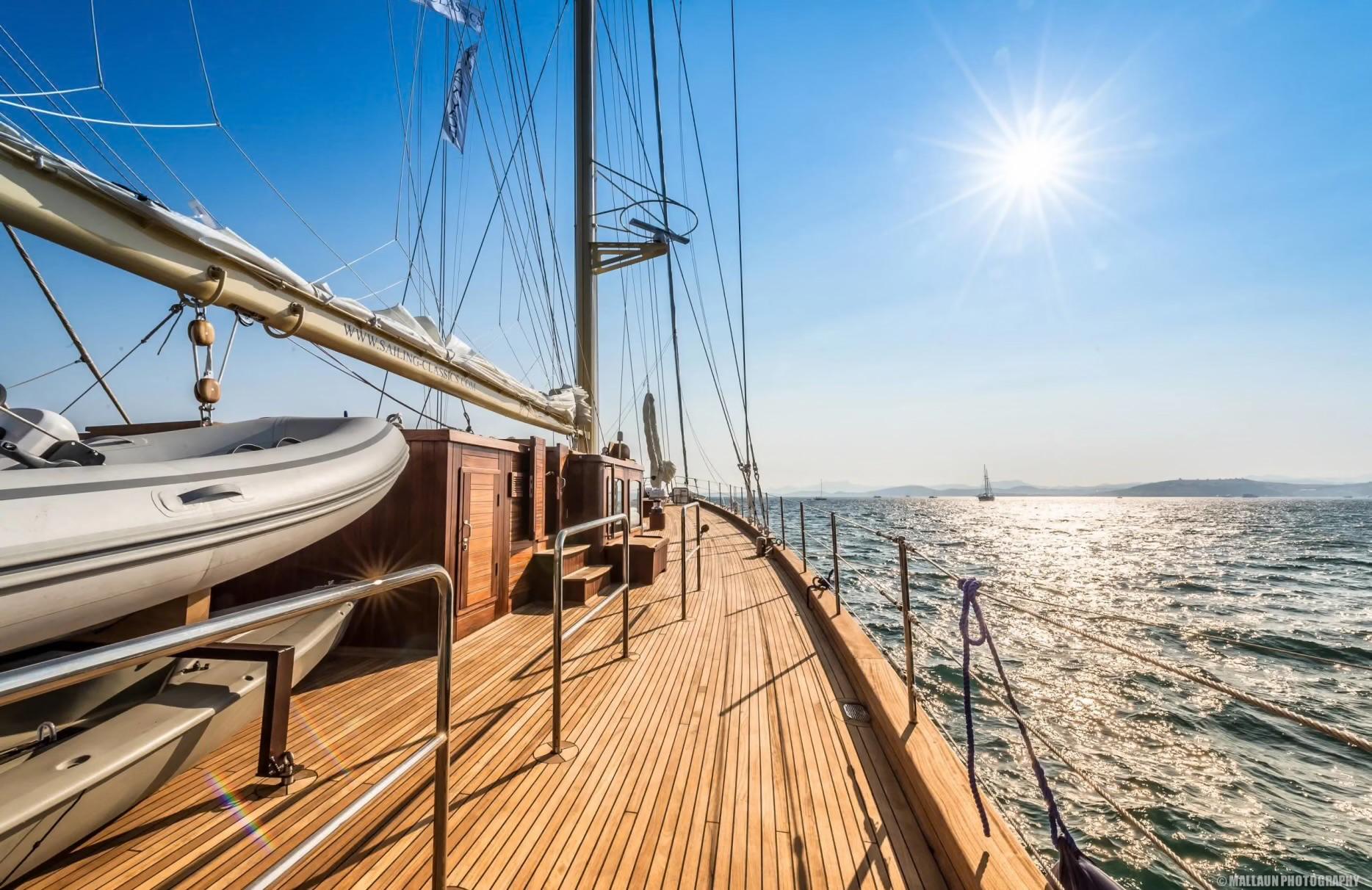 gulet side deck with teak planking, white tender, mast rigging and open sea view