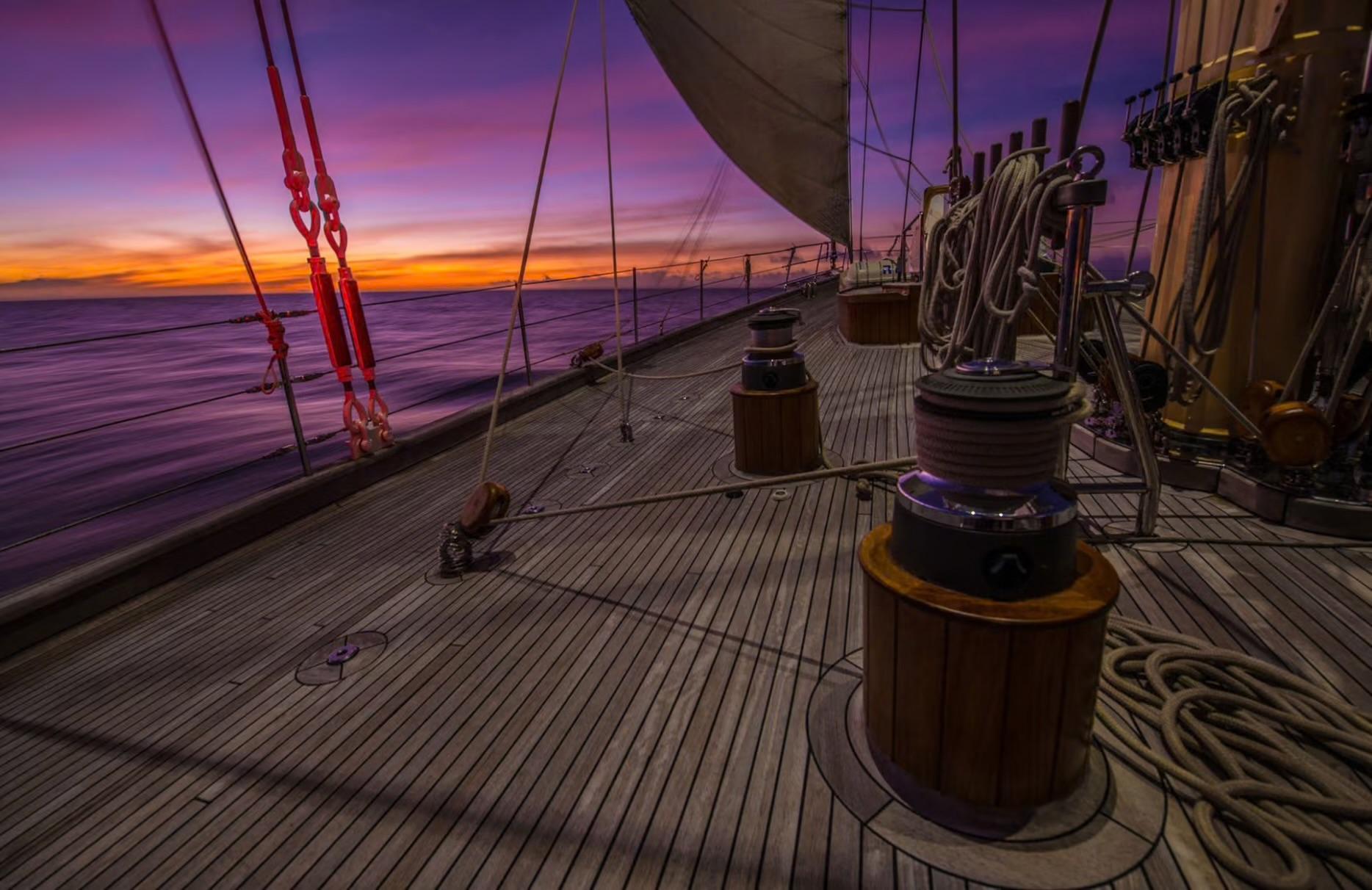 wooden deck of sailing yacht with winches, rigging and purple sunset sky