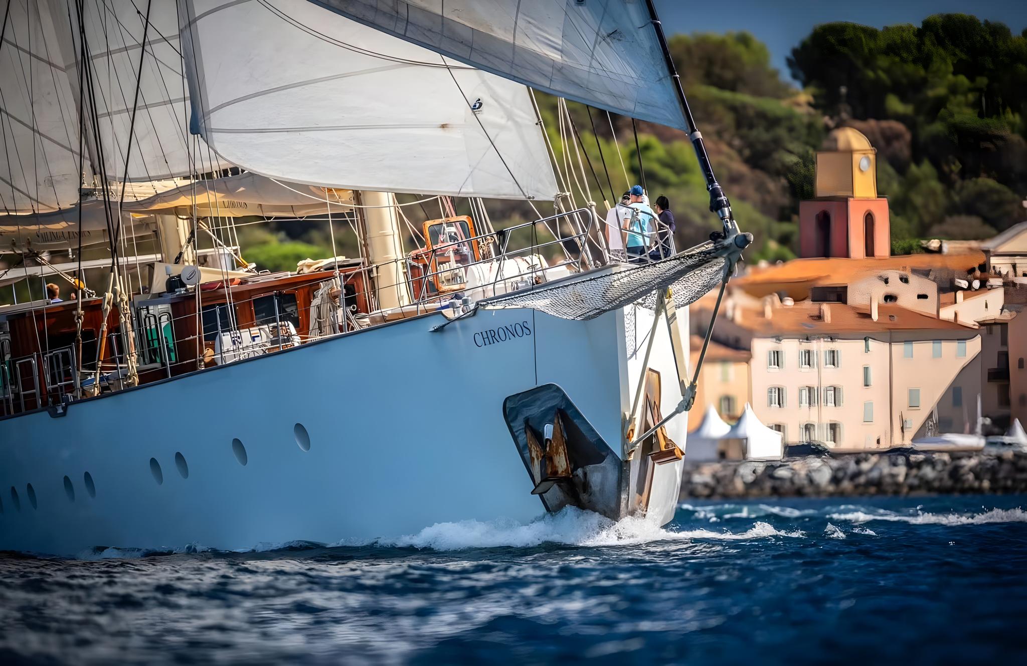 Traditional gulet yacht CHRONOS sailing with white sails near historic Mediterranean harbor town
