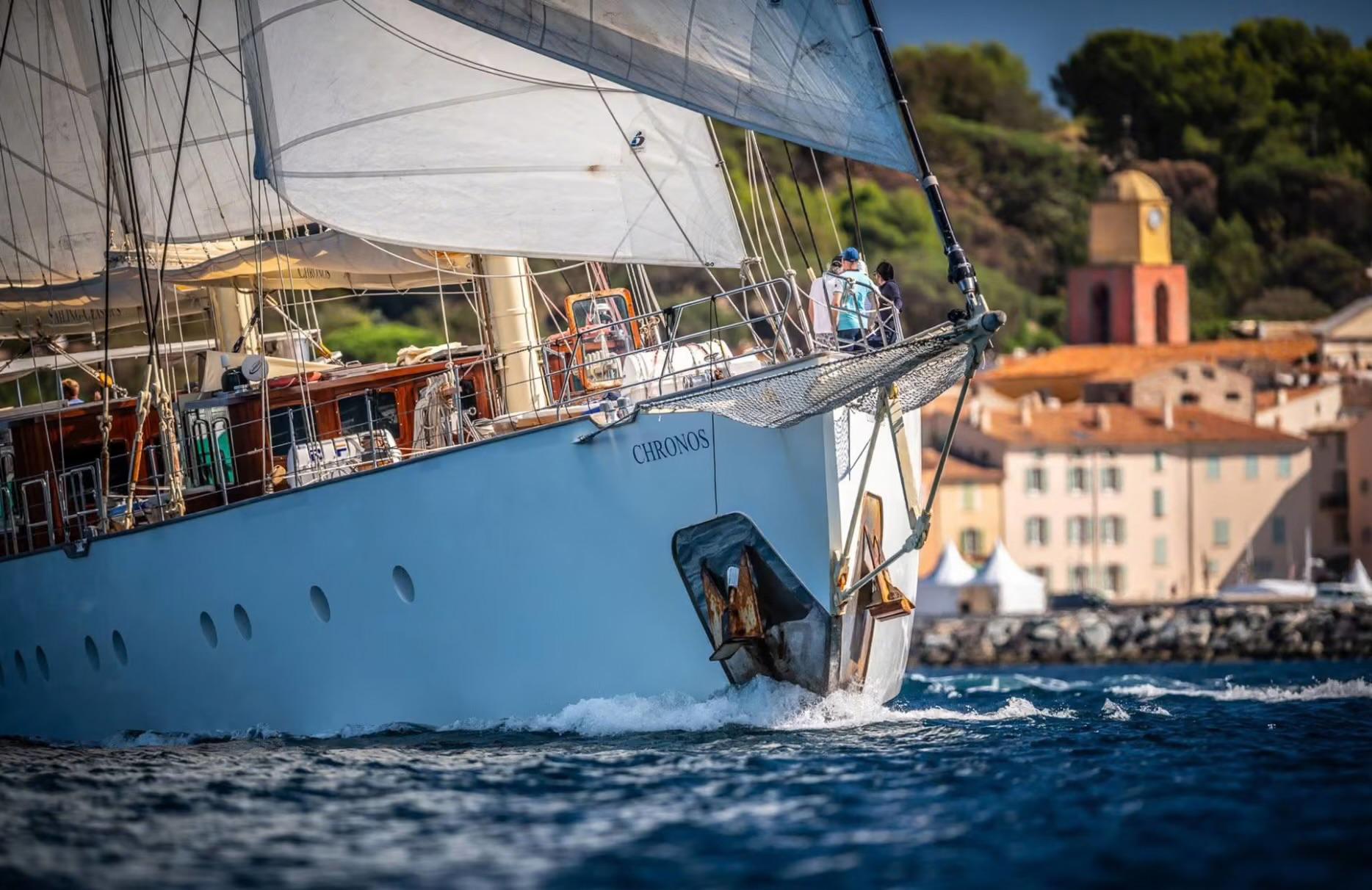 Traditional gulet yacht CHRONOS sailing with white sails near historic Mediterranean harbor town