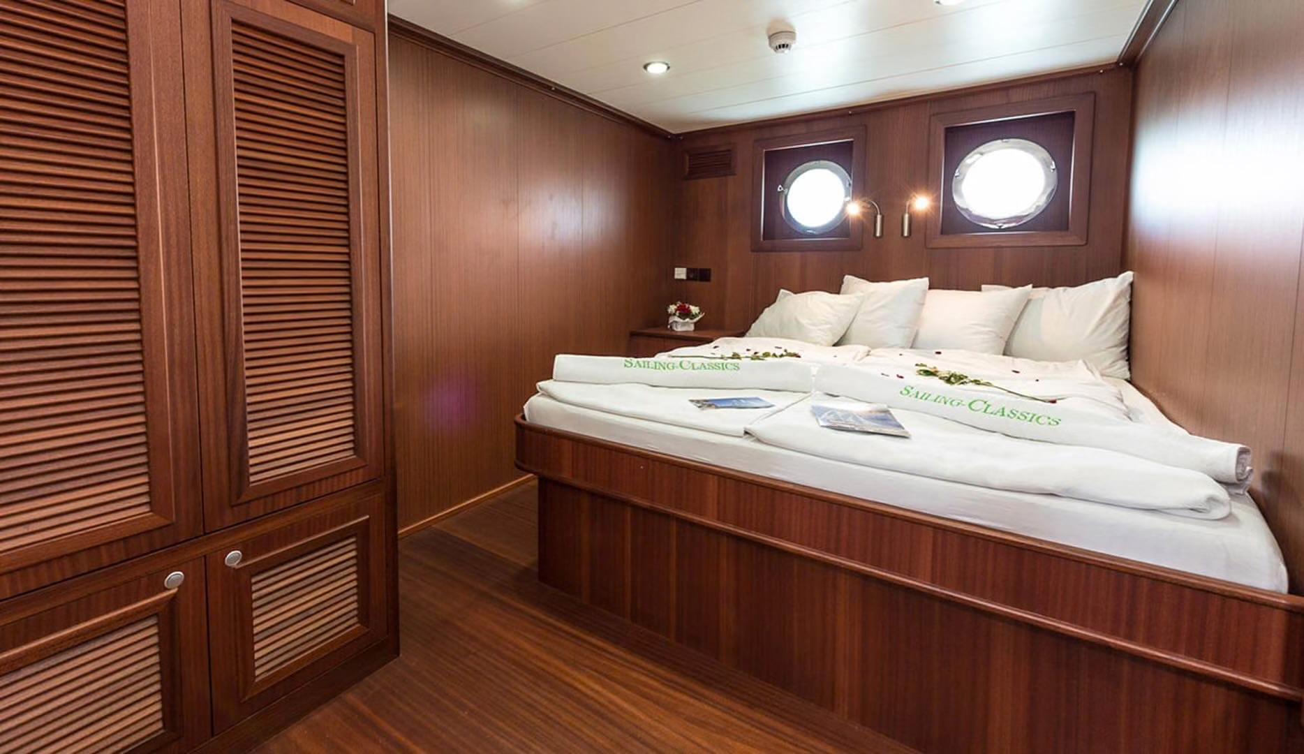 yacht guest cabin with double bed, wooden paneling, two portholes and wardrobe storage