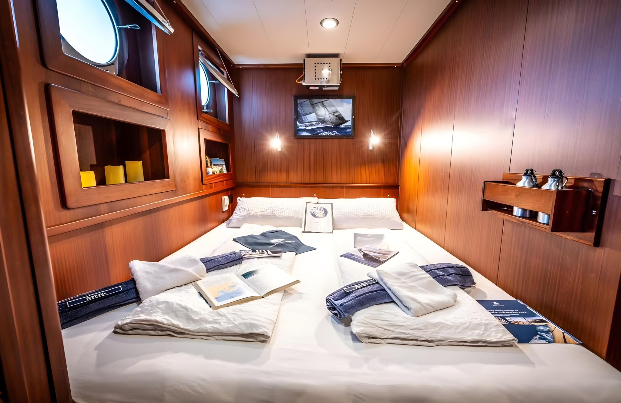 yacht cabin interior with double bed, wood paneling, portholes, and built-in storage compartments