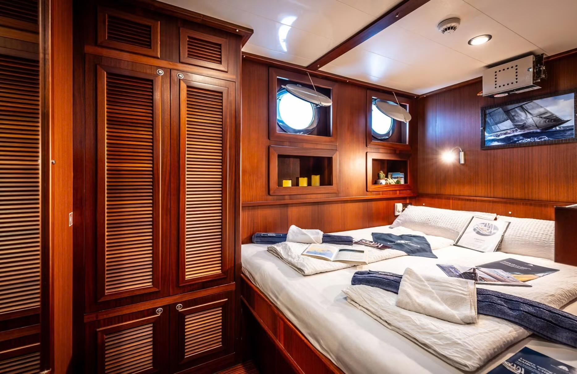 yacht guest cabin featuring double bed with navy towels and extensive teak wardrobe storage