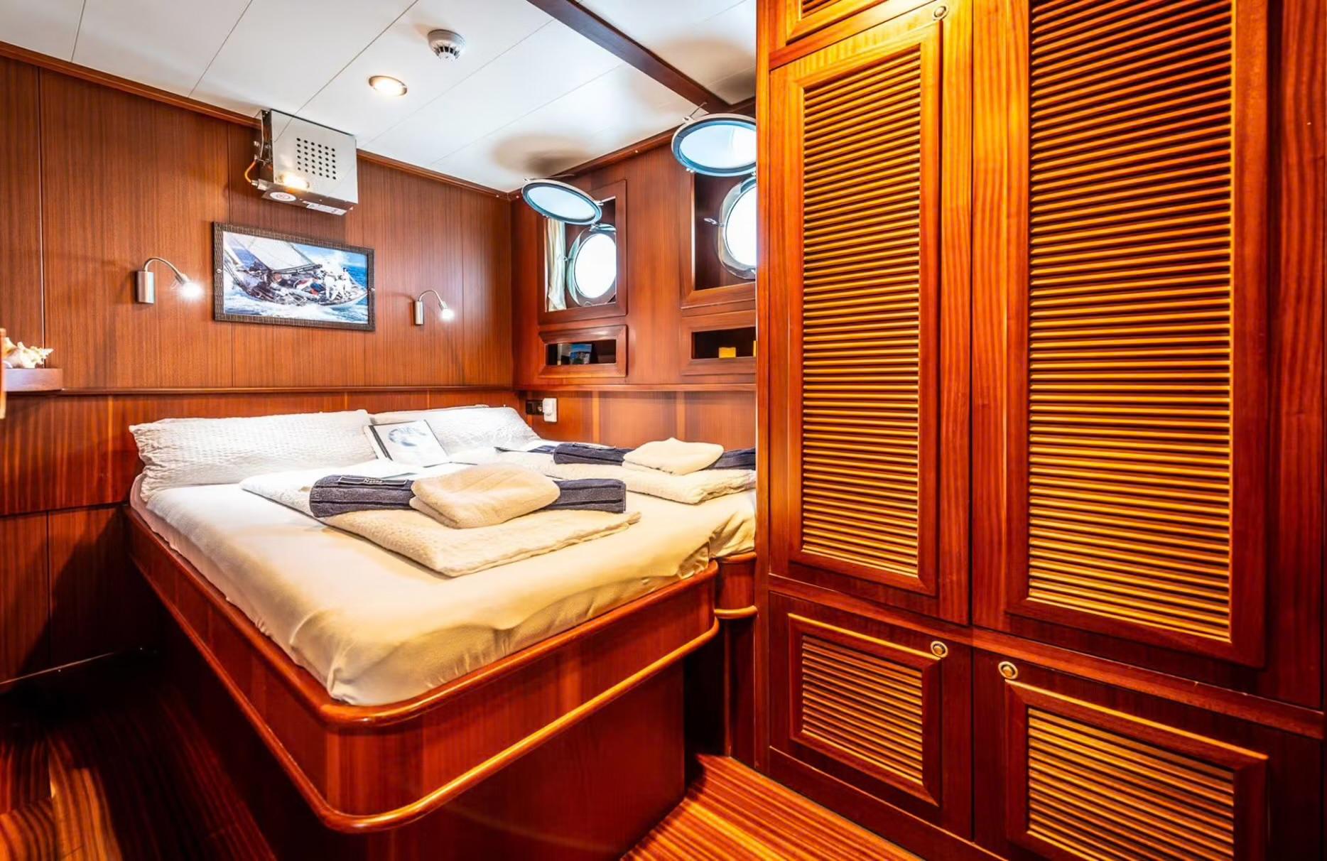 yacht guest cabin with double bed, wooden paneling, portholes and louvered wardrobes