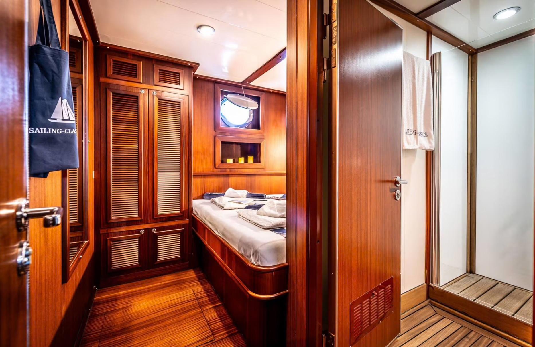 yacht guest cabin with single bed, built-in storage, porthole window, and rich wood paneling