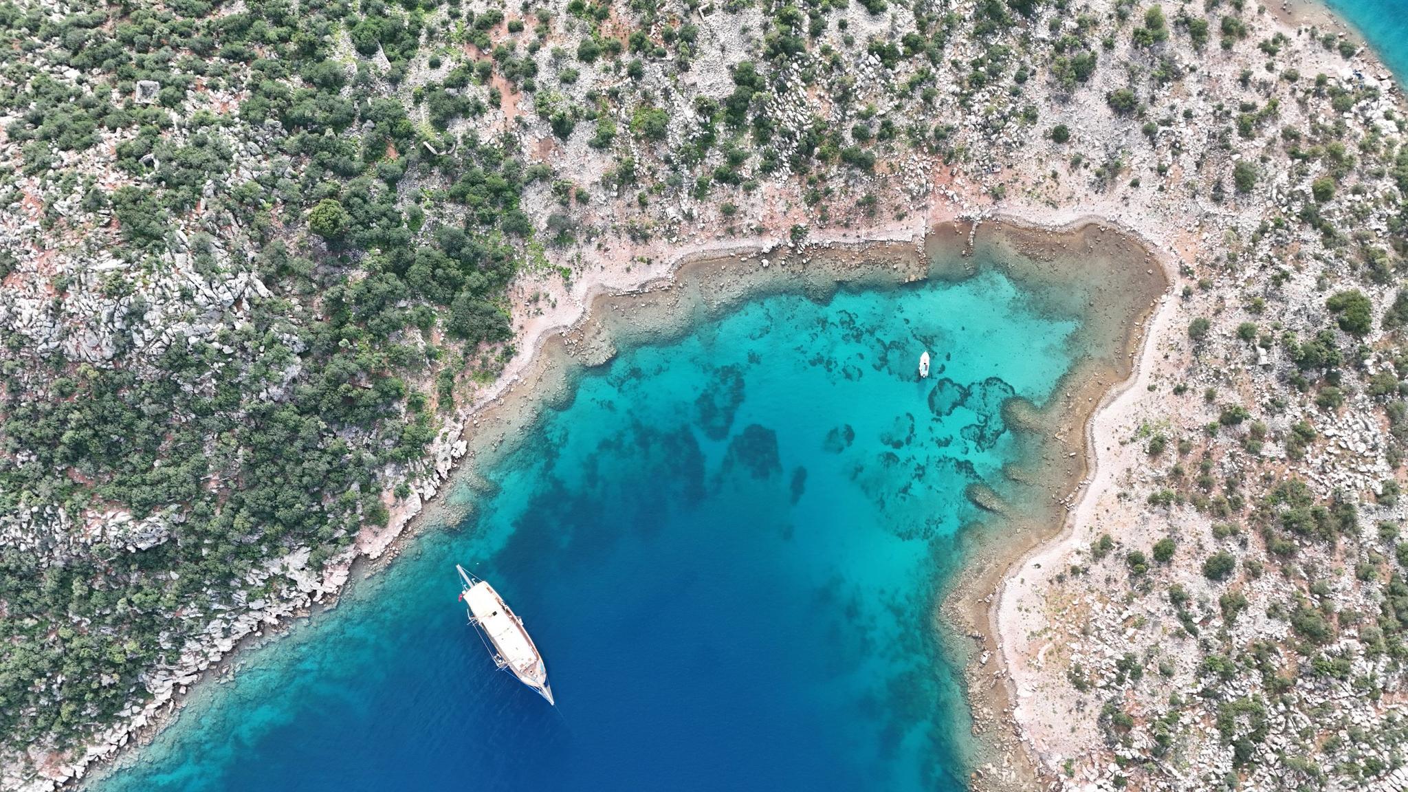 aerial view of white gulet yacht anchored in pristine turquoise bay surrounded by rocky coastline