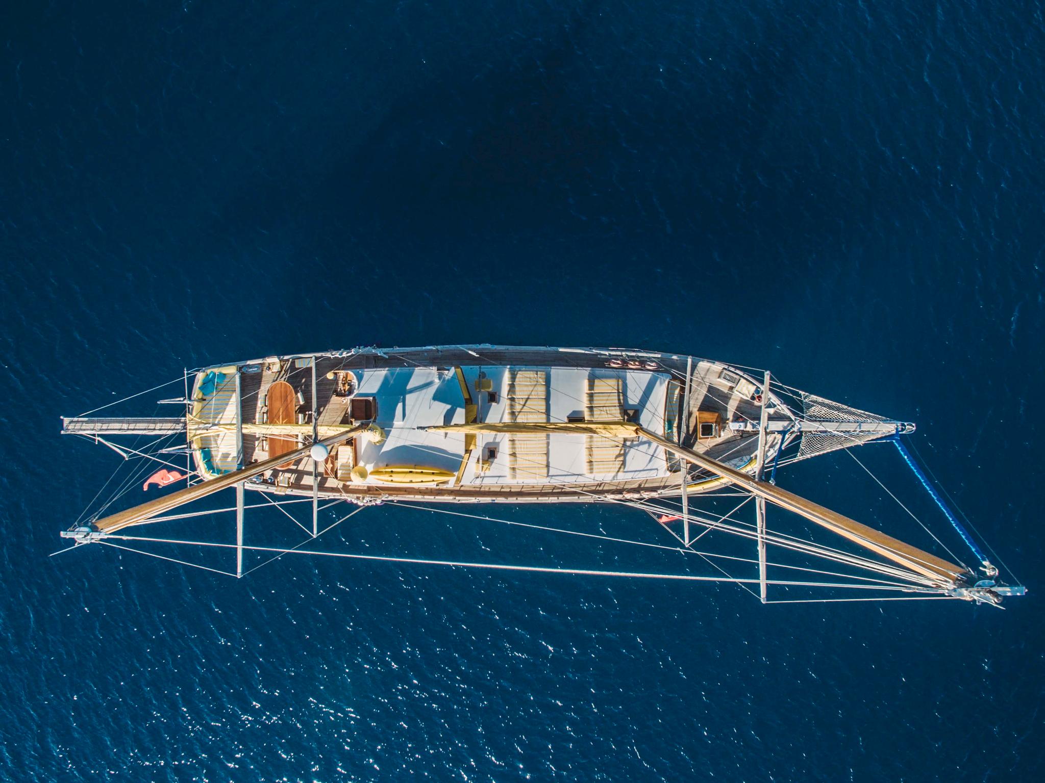 aerial drone shot of traditional sailing yacht with white deck at anchor in deep blue water