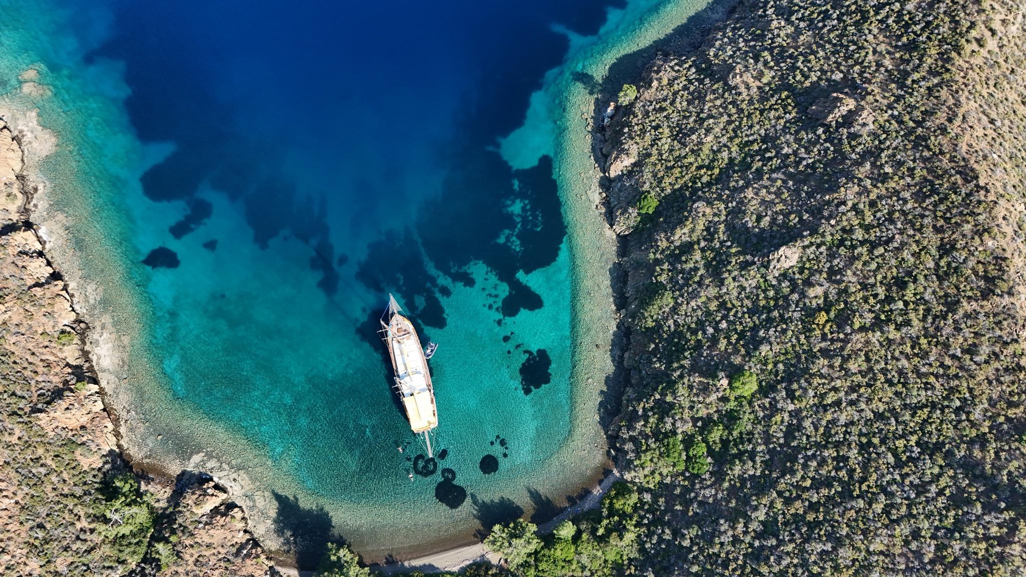aerial view of white gulet yacht anchored in crystal clear turquoise bay surrounded by rocky coastline