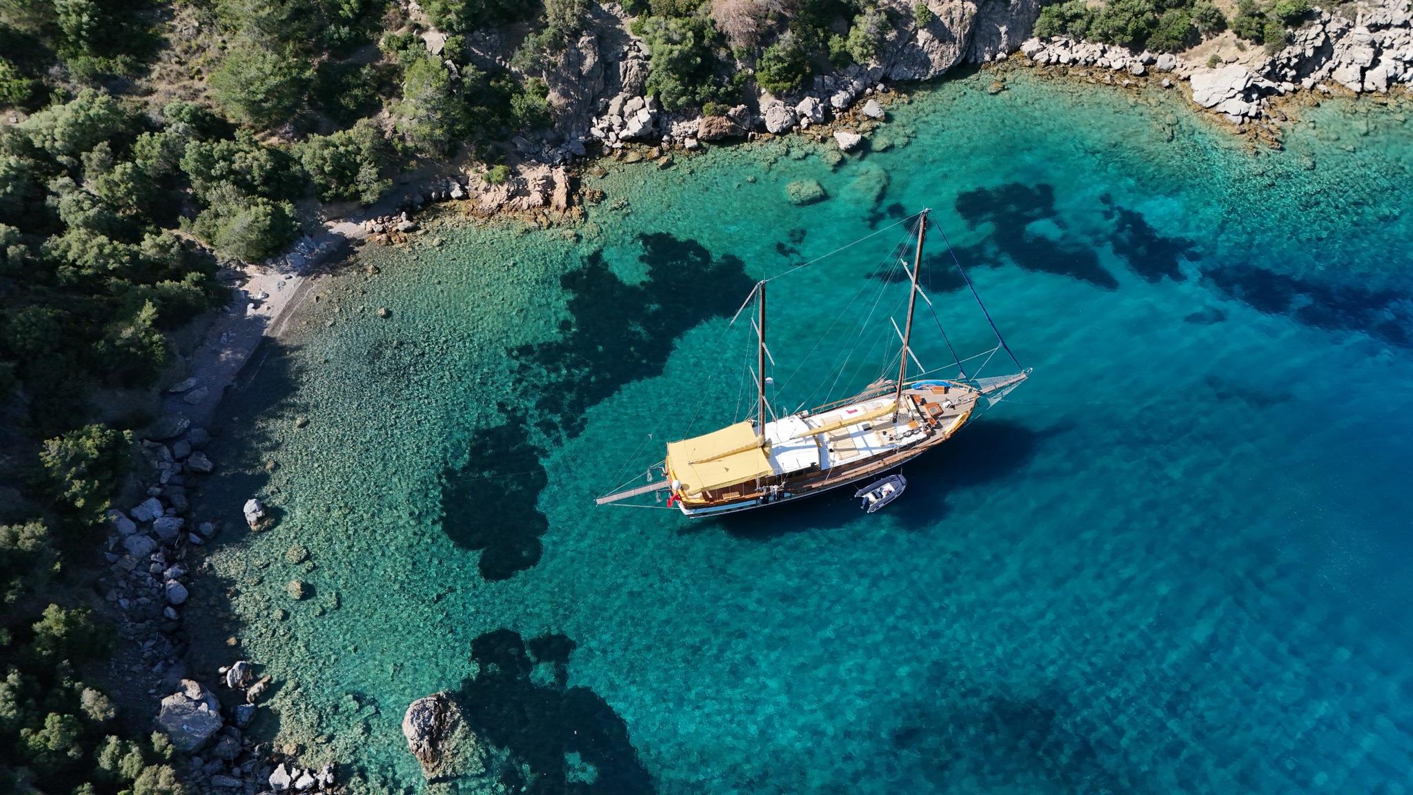 aerial view of wooden gulet yacht anchored in crystal clear turquoise bay with rocky coastline