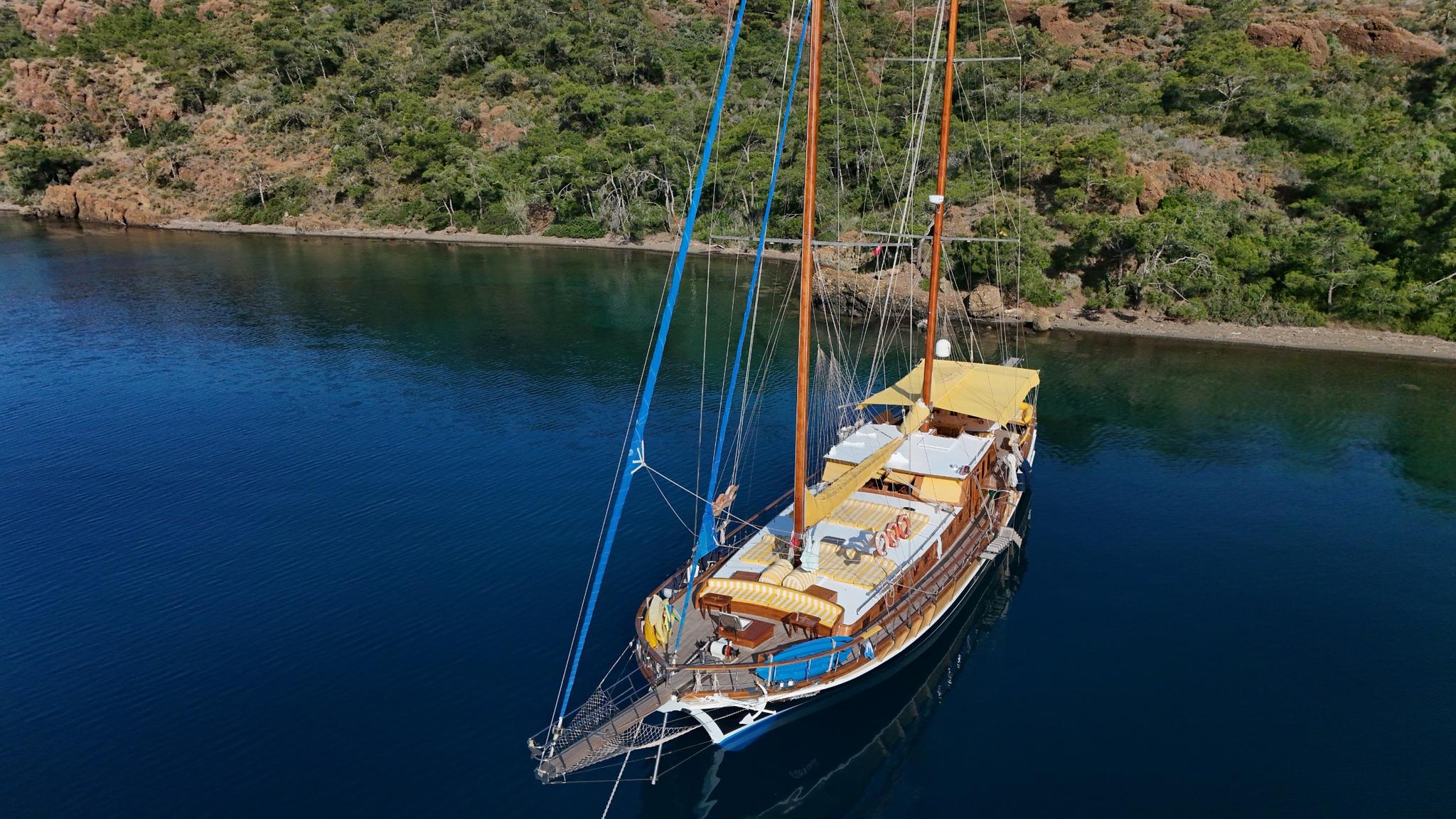 aerial view of traditional wooden gulet with two masts anchored in turquoise bay