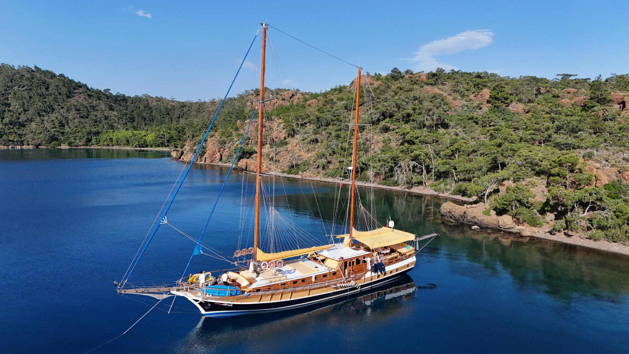 aerial view of traditional wooden gulet yacht anchored in calm turquoise bay surrounded by forested hills
