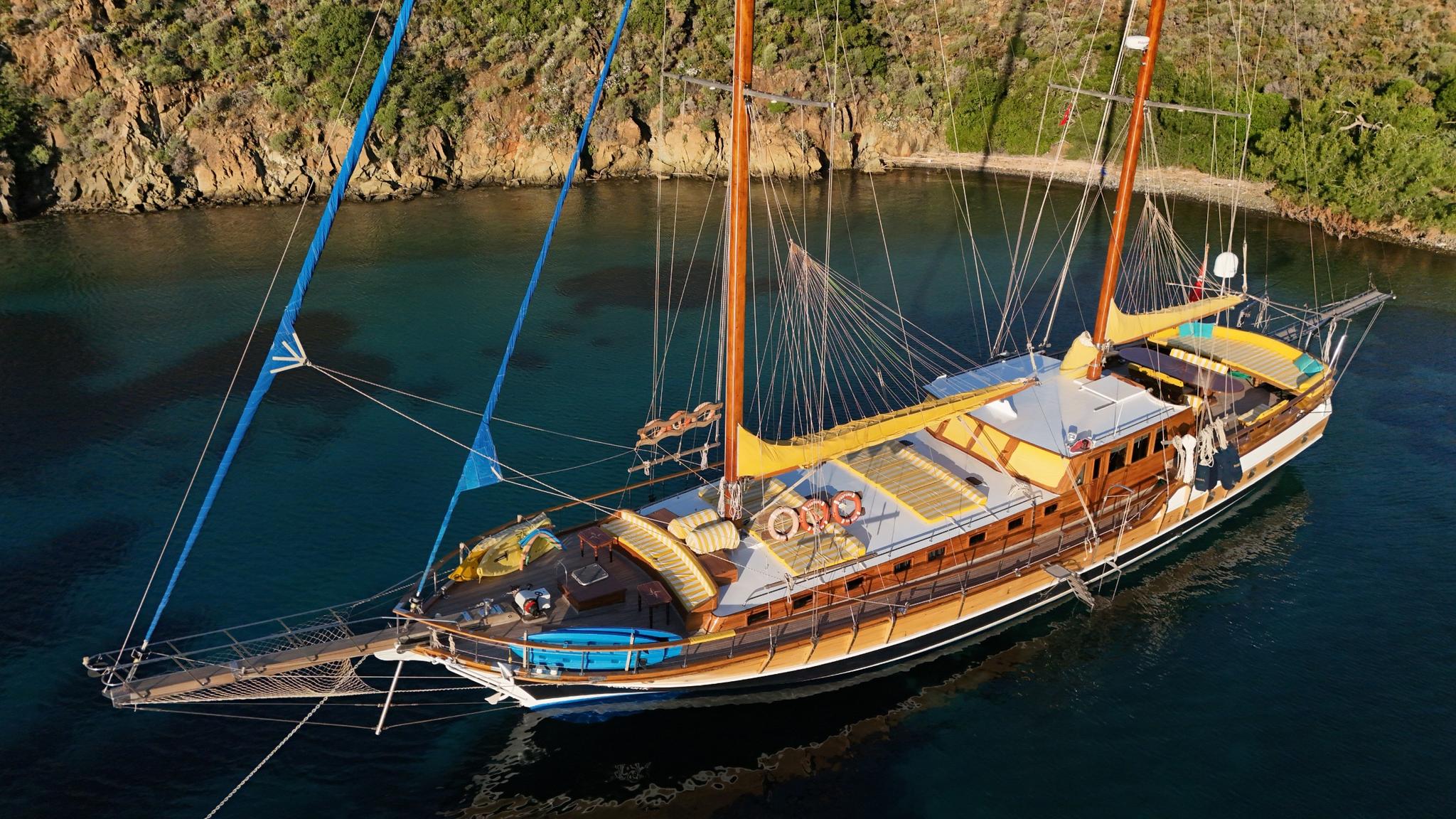 aerial view of traditional wooden gulet with orange masts anchored in secluded turquoise bay