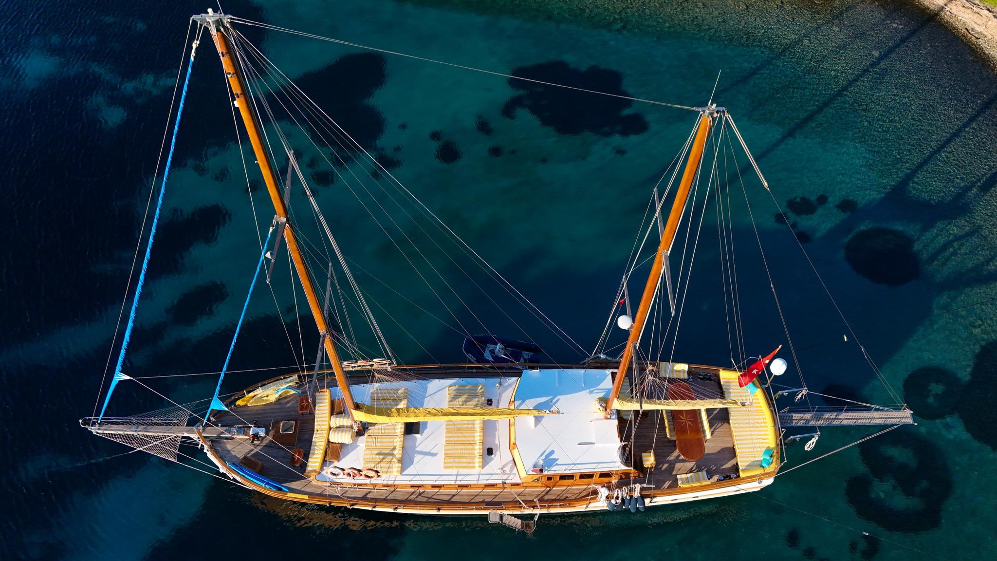 aerial view of traditional wooden gulet with two masts anchored in crystal clear turquoise bay