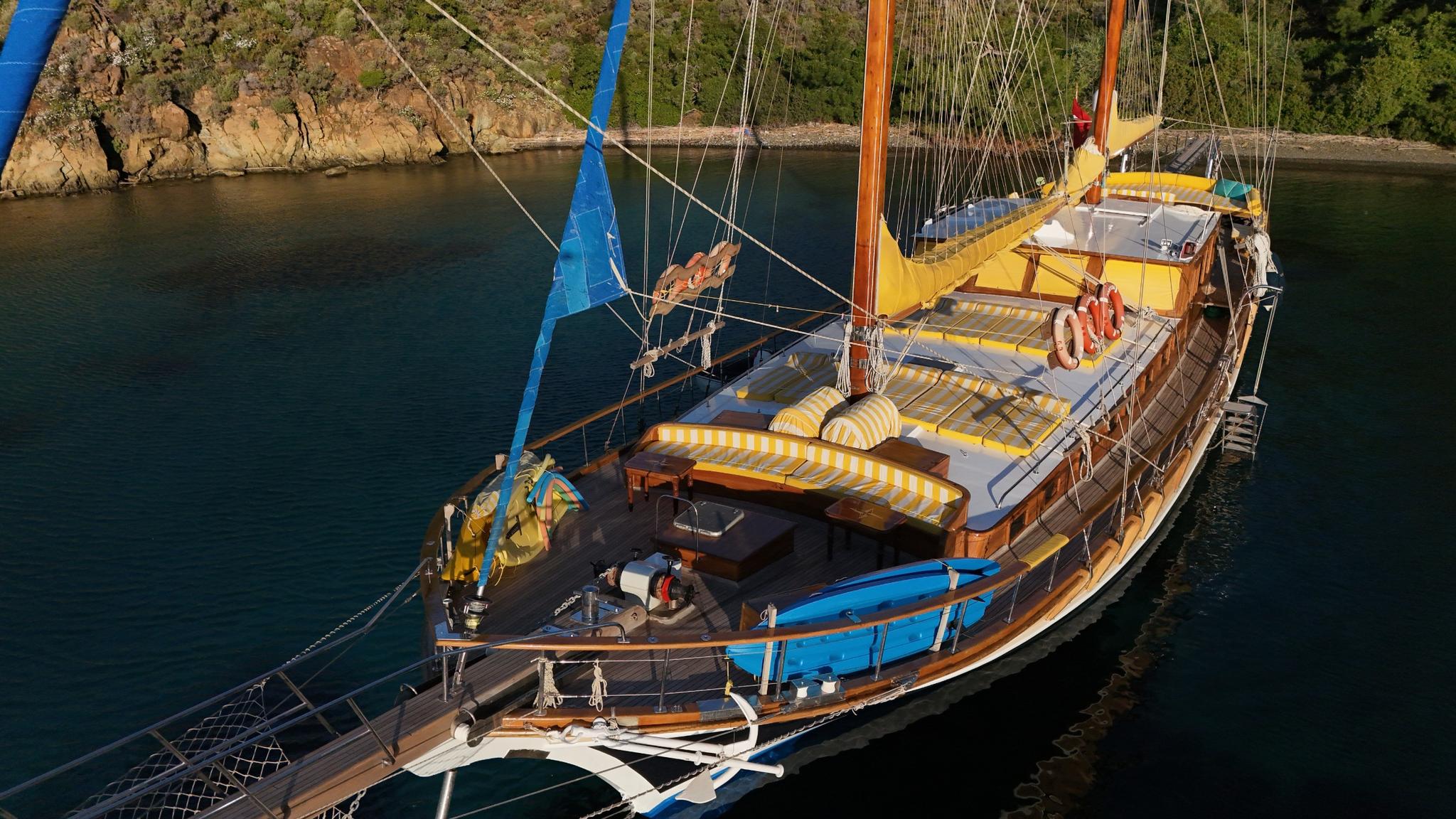aerial view of traditional wooden gulet with yellow sunshades anchored in turquoise bay