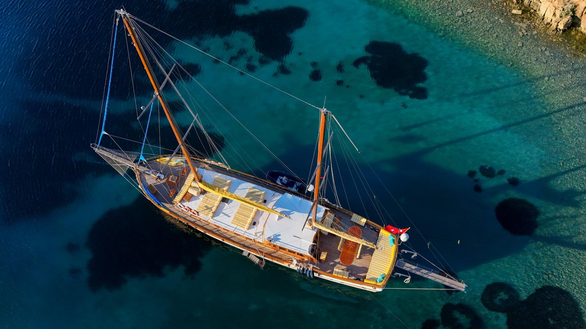 aerial view of wooden gulet yacht anchored in turquoise Mediterranean waters near rocky coastline