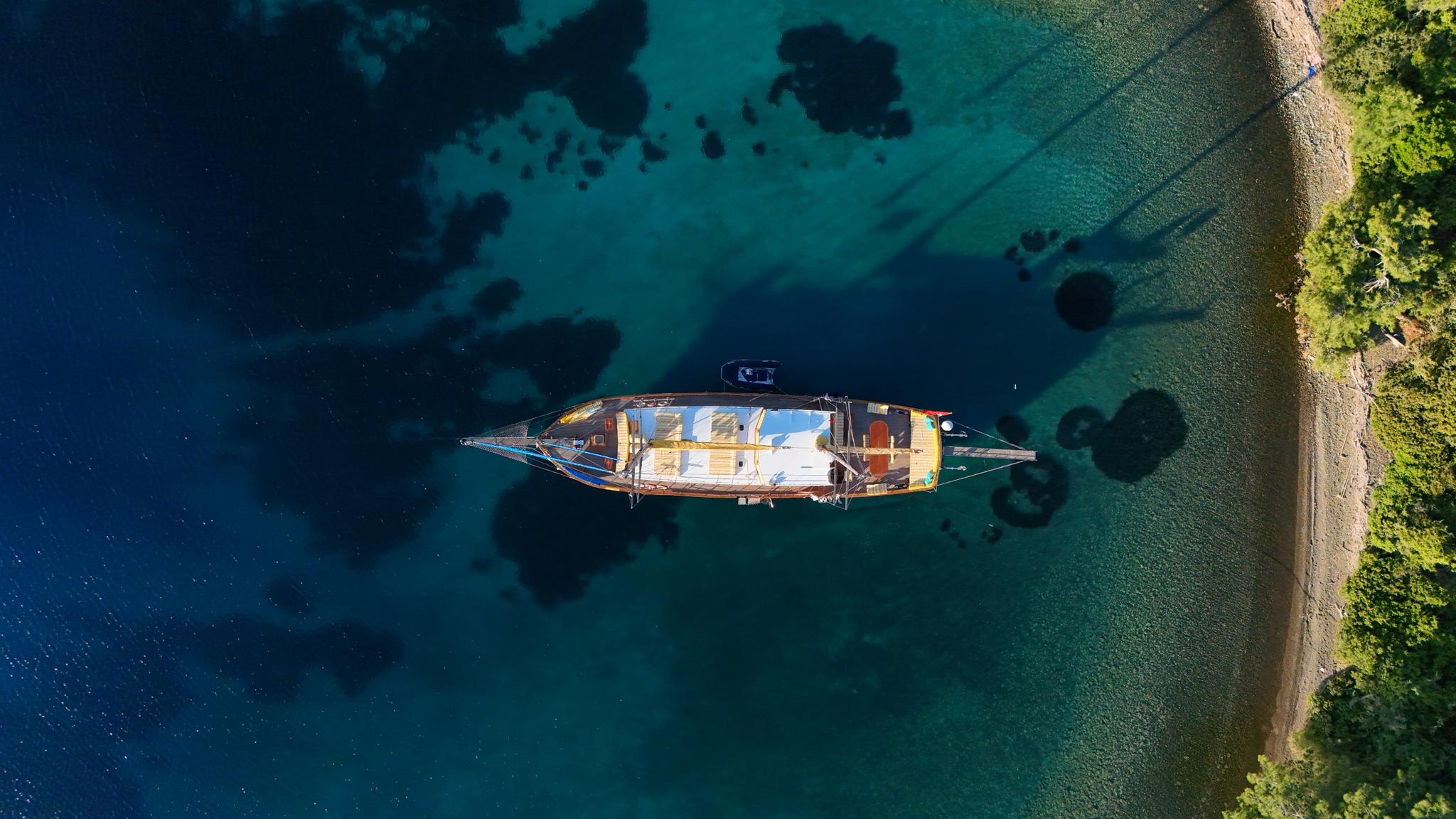 aerial view of traditional wooden gulet anchored in crystal clear turquoise waters near green coastline