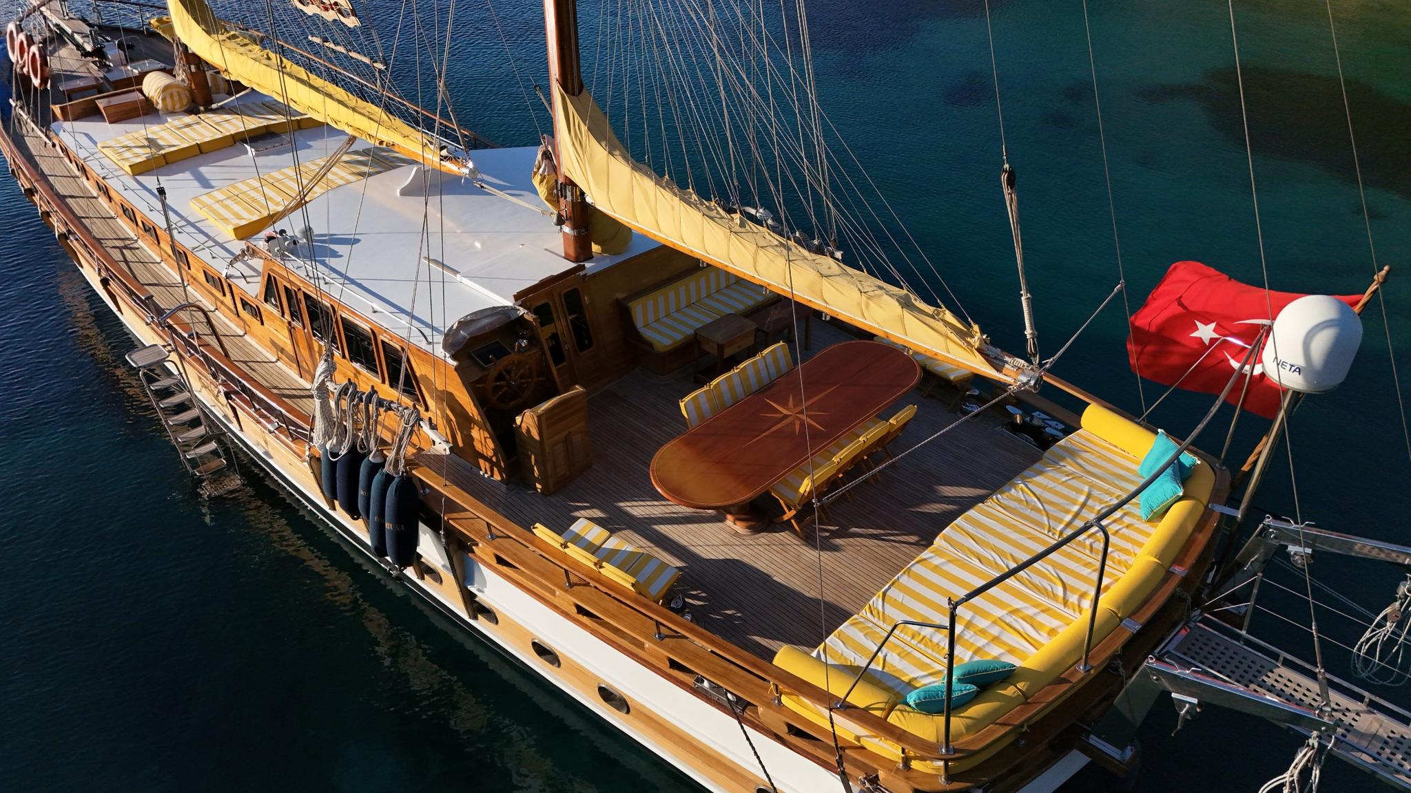 traditional wooden gulet deck featuring oval dining table with umbrella and yellow striped sun loungers