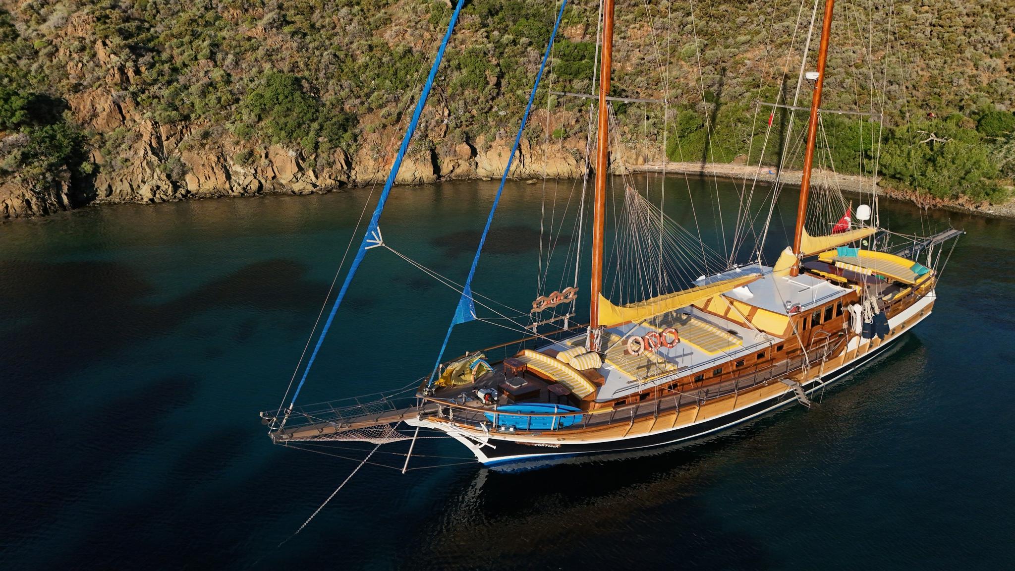 aerial view of wooden gulet with yellow and blue awnings anchored in turquoise bay