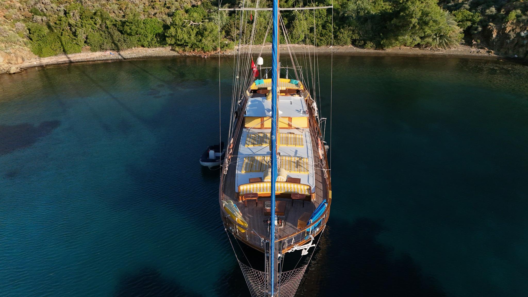 aerial view of traditional wooden gulet yacht with blue mast anchored in secluded turquoise bay