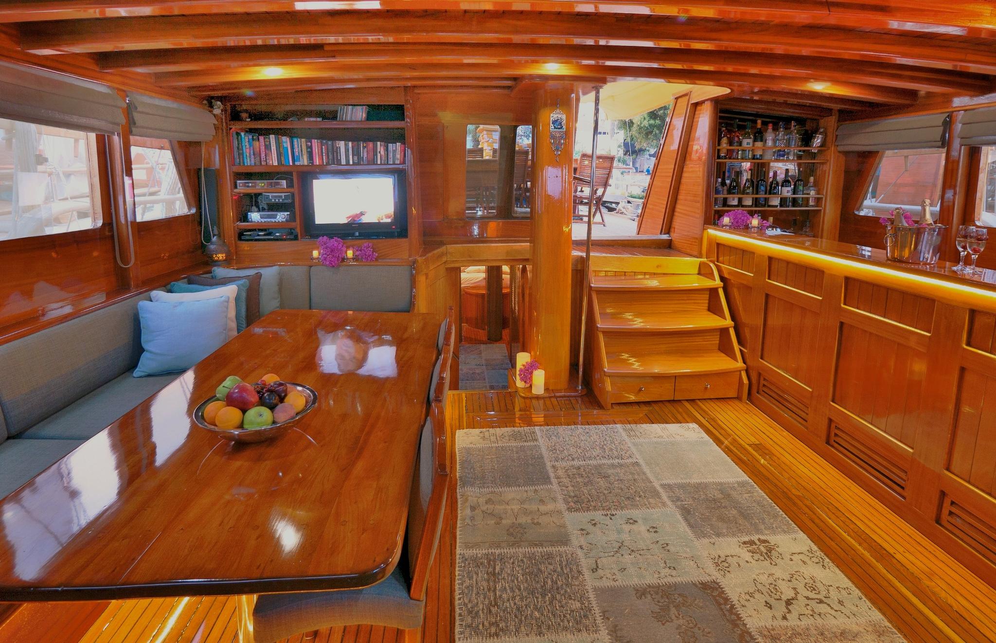 yacht main salon with L-shaped seating, dining table, built-in bar and entertainment center