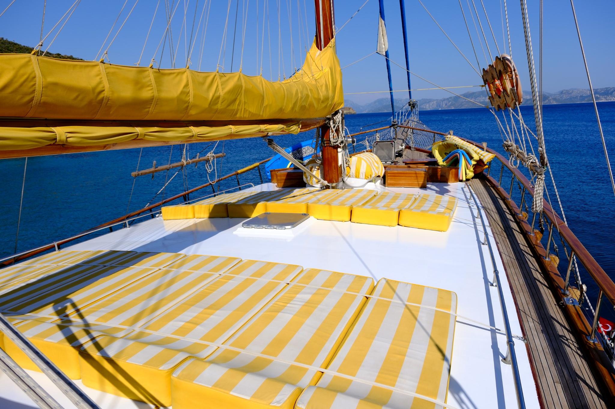 gulet bow deck featuring yellow and white striped sun cushions with traditional sailing rigging