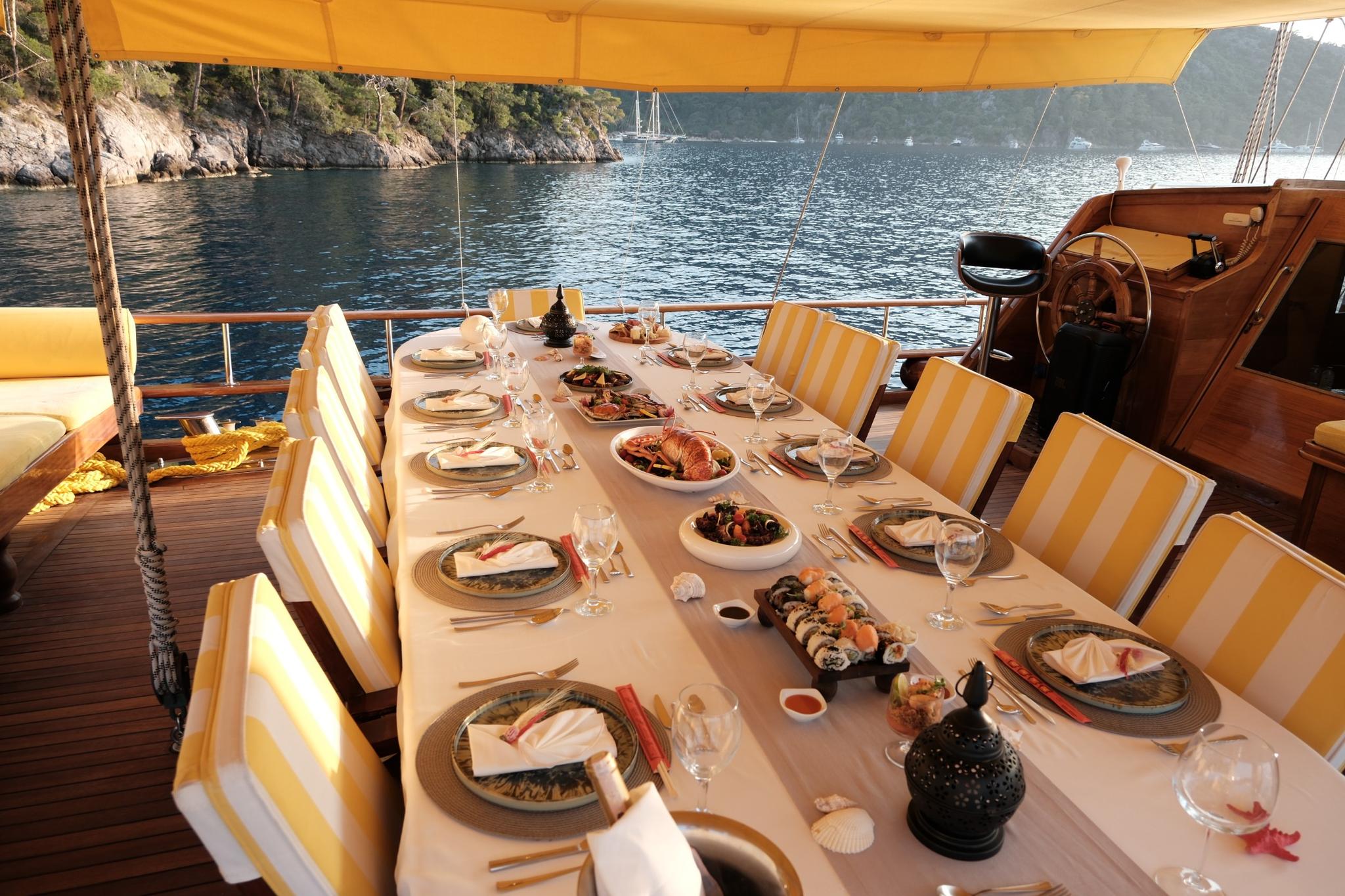 yacht aft deck dining table set with sushi, seafood dishes and wine glasses