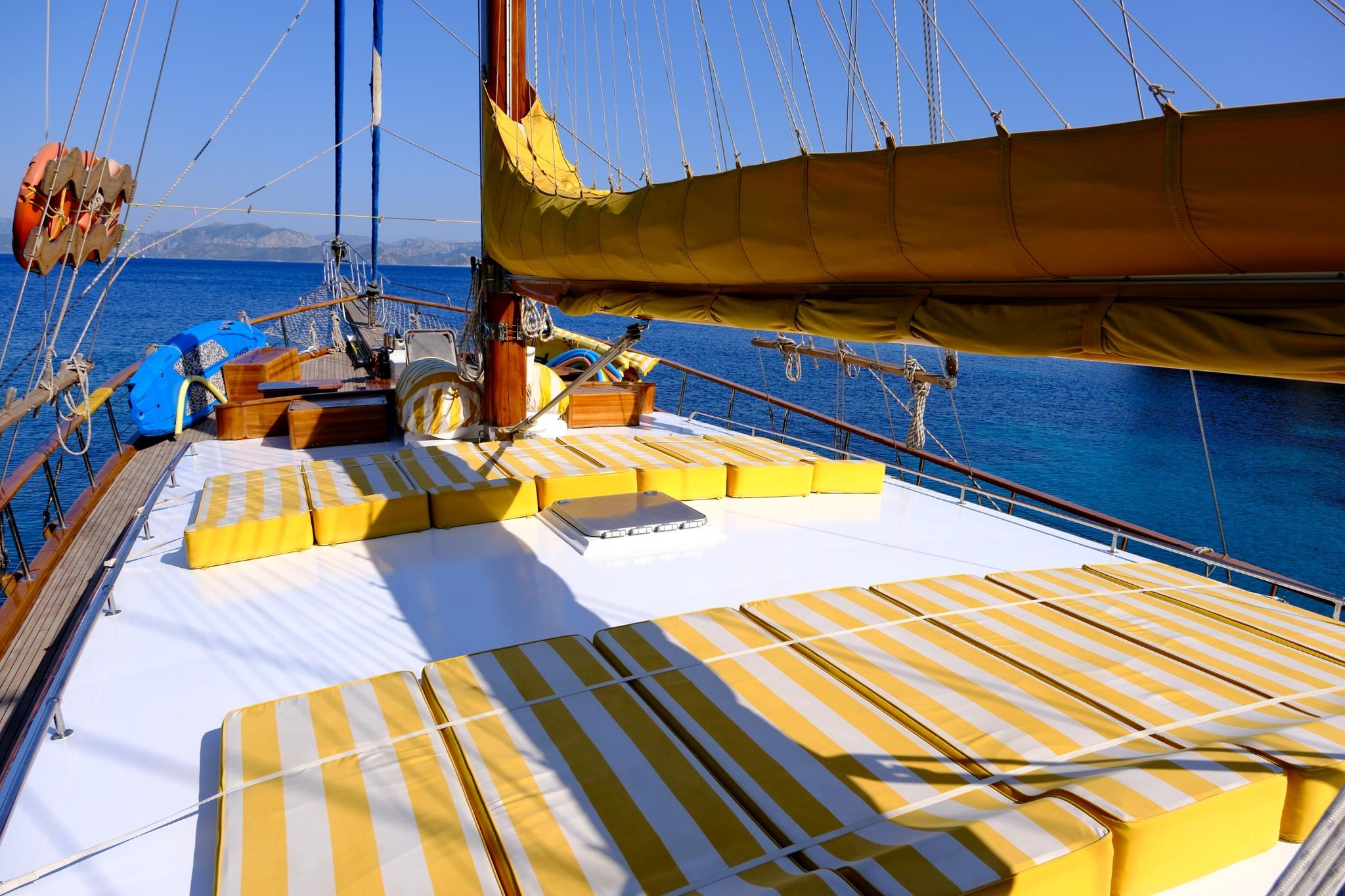 gulet bow deck featuring yellow and white striped sun cushions with sailing rigging overhead