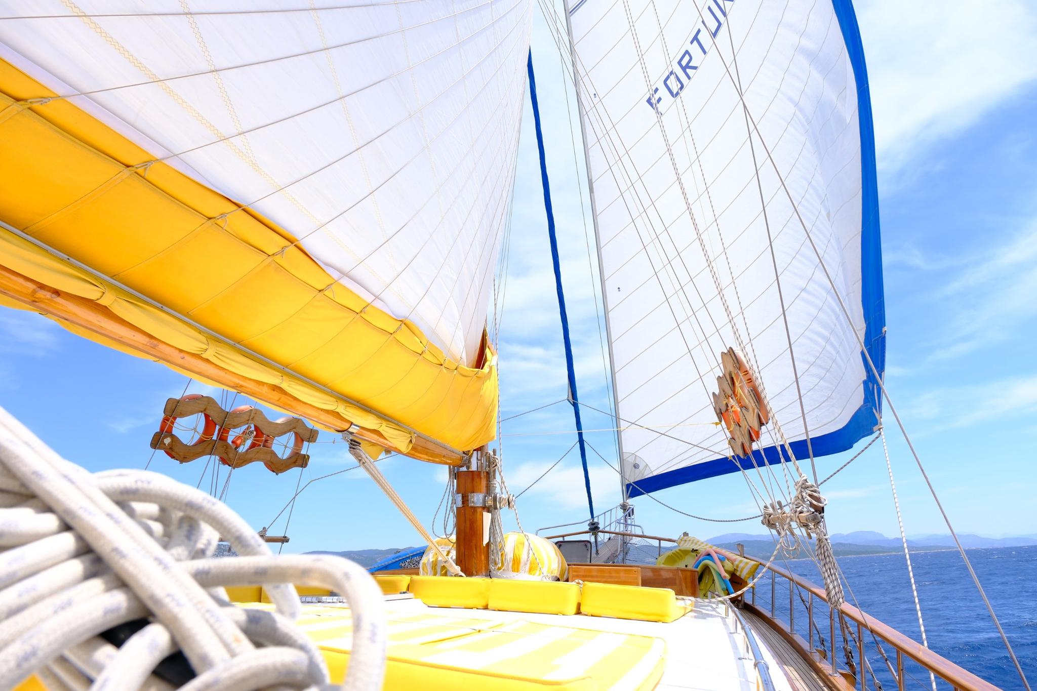 sailing yacht deck view with yellow boom, white sails, and blue Mediterranean waters