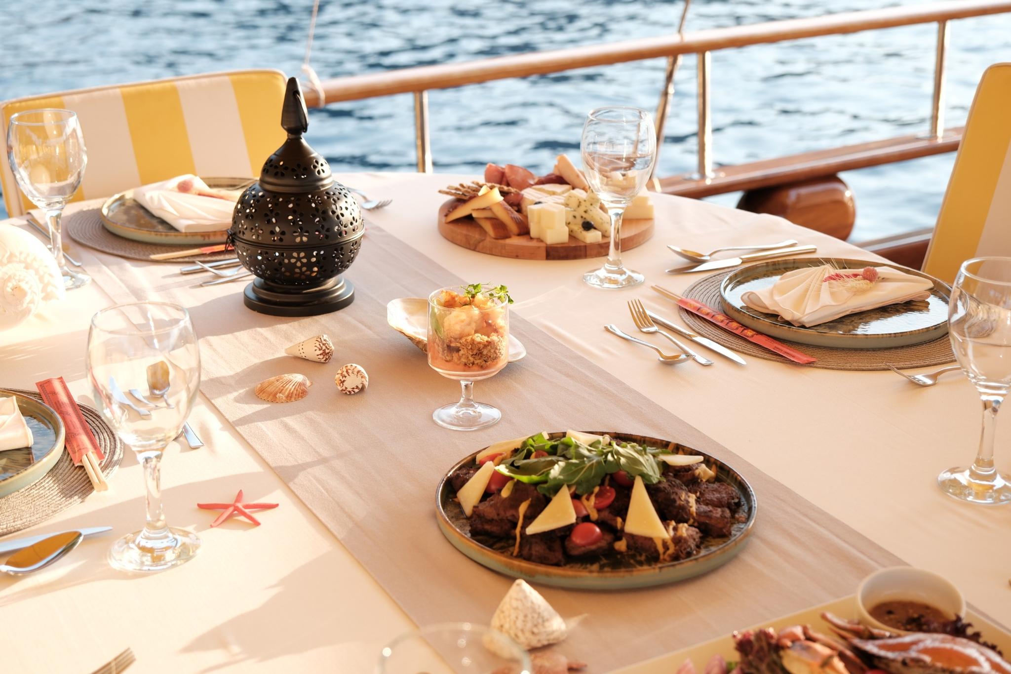 yacht aft deck dining table with plated meal, cheese board, wine glasses and decorative lantern