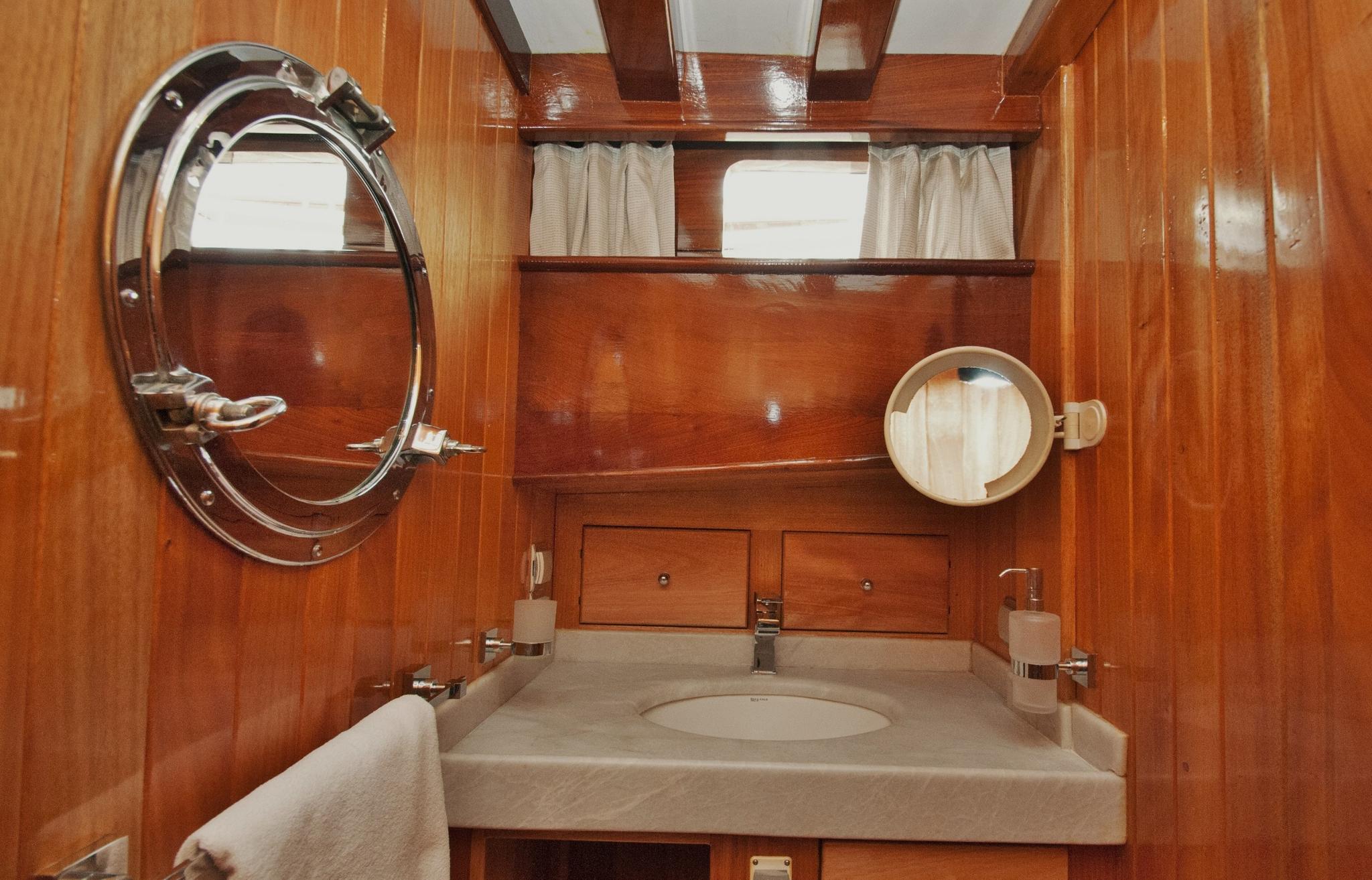 yacht bathroom featuring marble vanity, round porthole mirror, and warm wood paneling