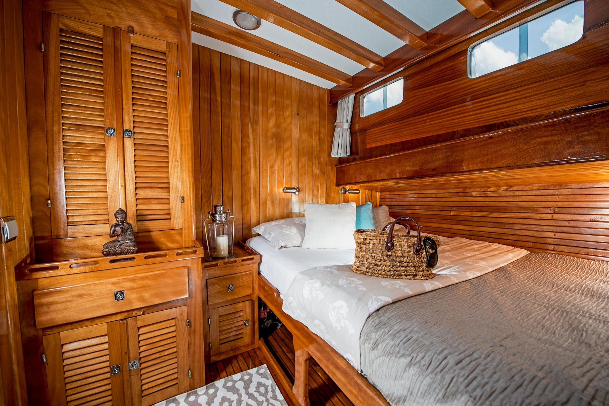 guest cabin featuring double bed with white linens, extensive wooden storage cabinets, and porthole windows