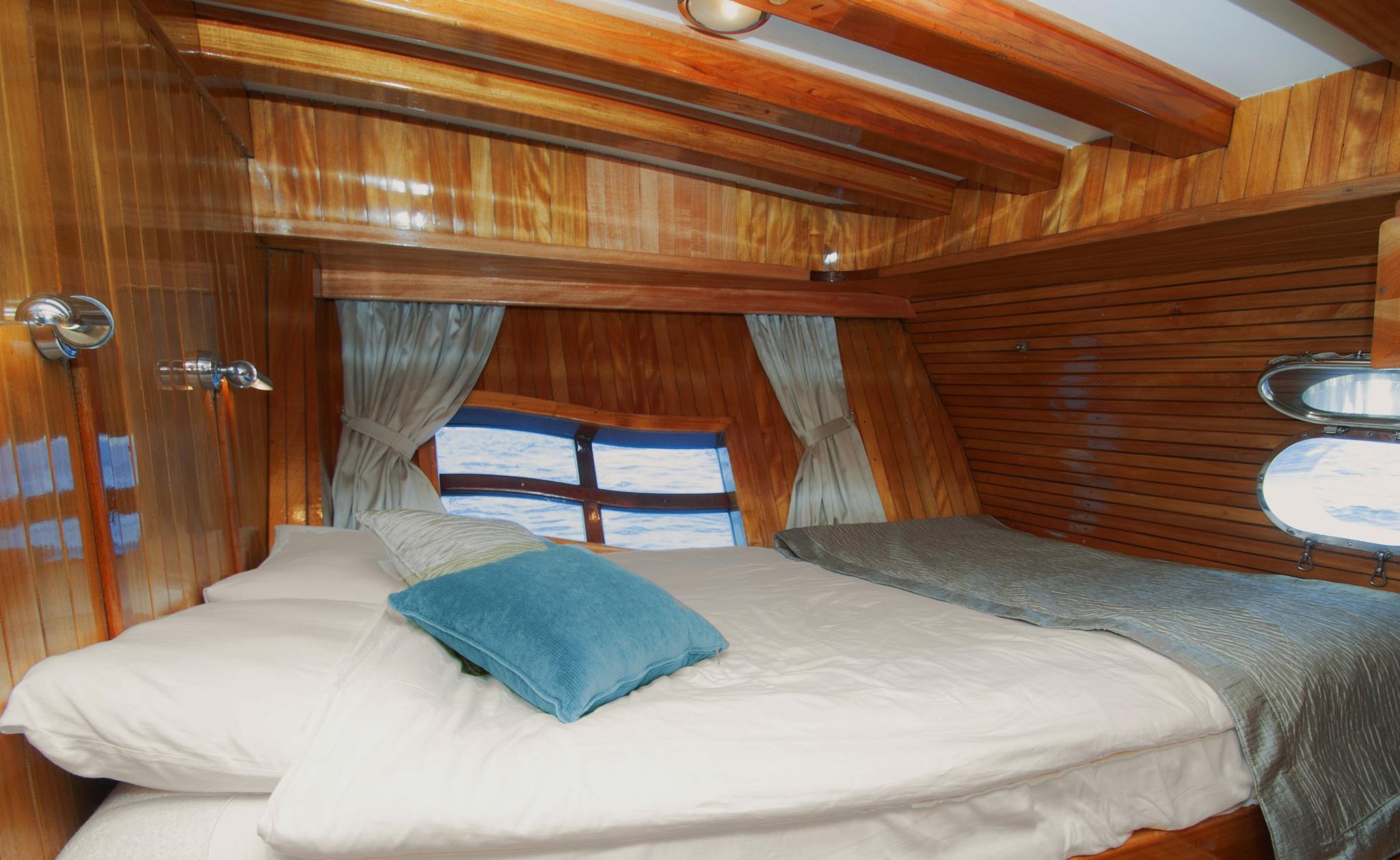 yacht cabin interior with white bedding, blue accent pillow, wooden paneling and porthole windows