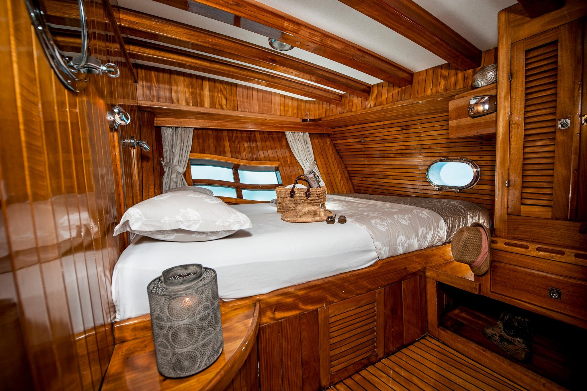 guest cabin interior featuring double bed with white linens, rich teak paneling and nautical portholes