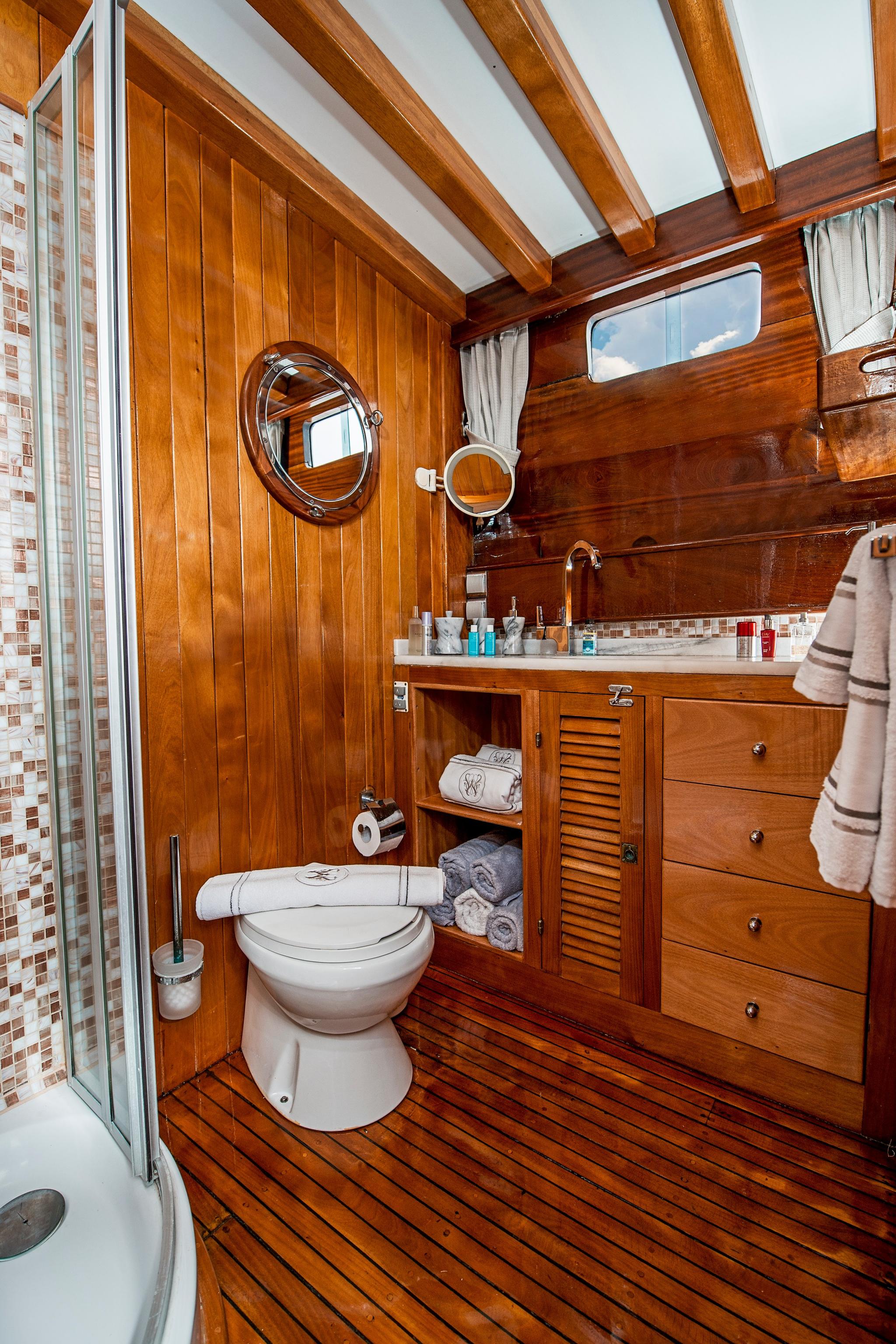 yacht bathroom with teak wood paneling, white toilet, vanity sink and mosaic tile shower