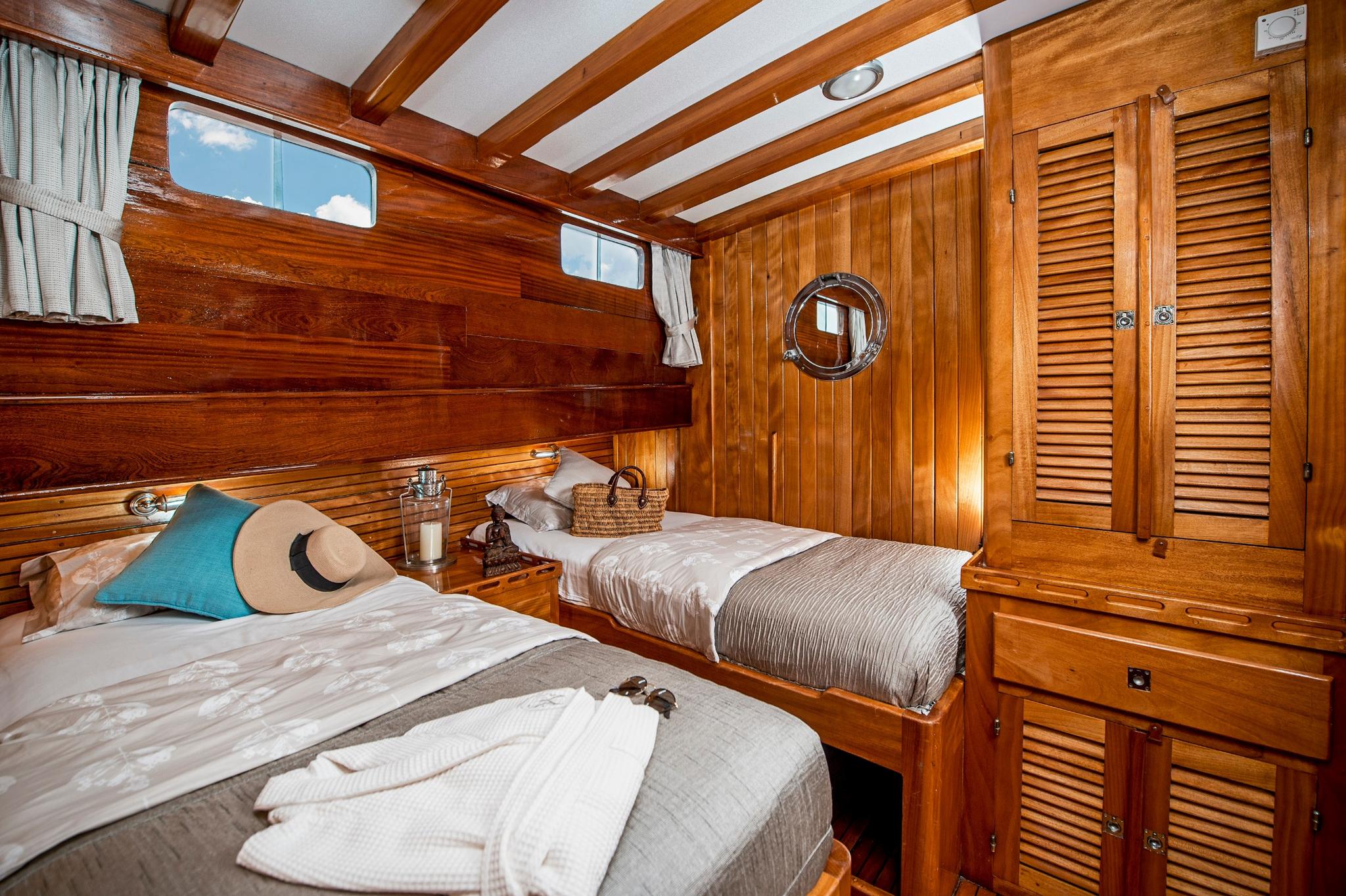 yacht guest cabin featuring twin beds, wooden paneling, portholes, and extensive built-in wardrobes