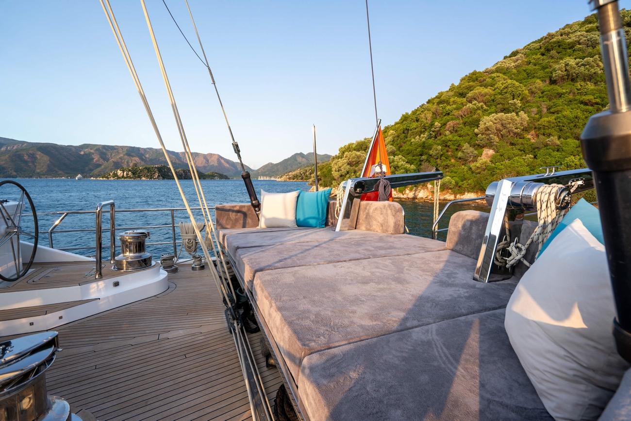 yacht aft deck with beige cushioned seating area and teak decking overlooking forested coastline