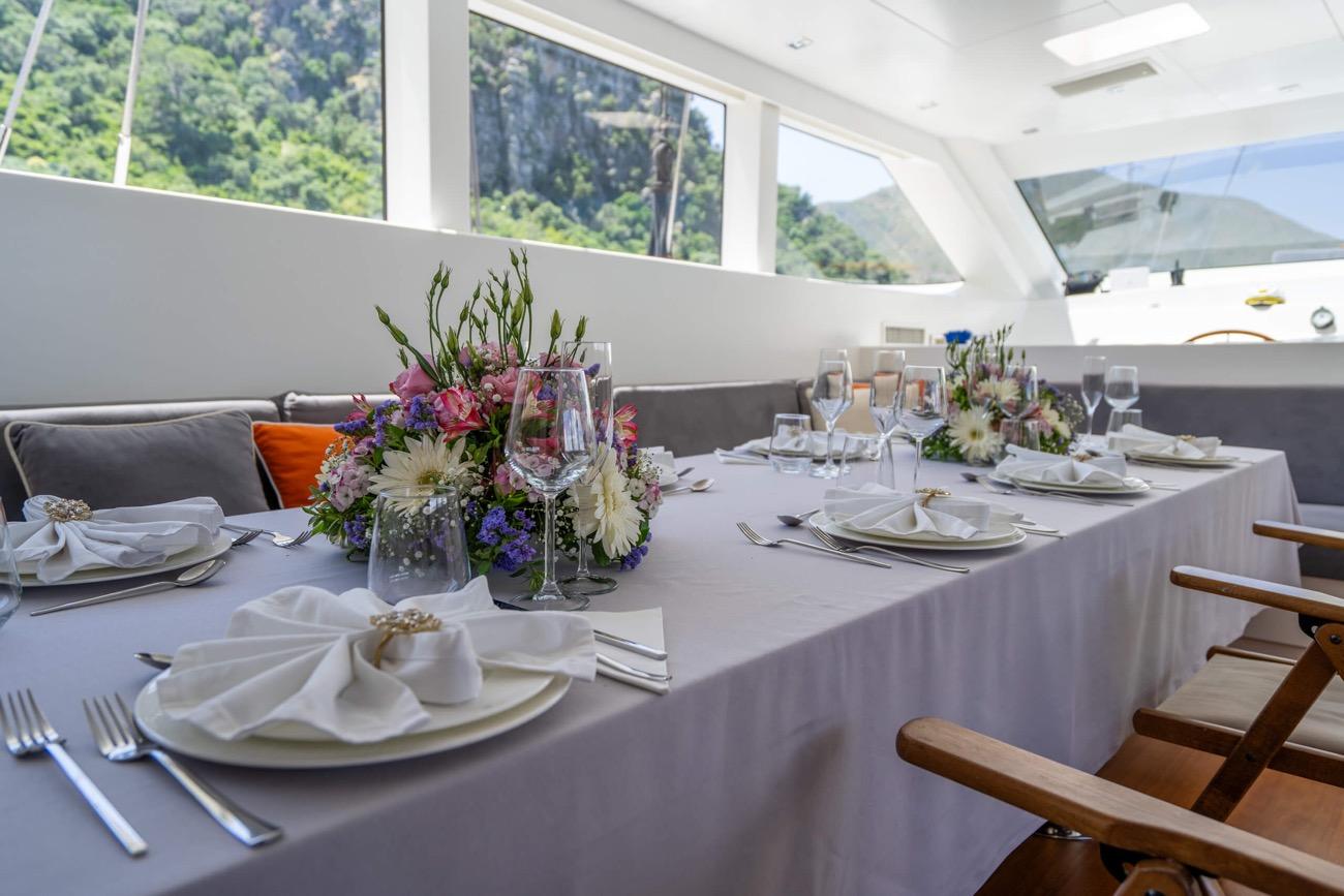 yacht salon dining area with white tablecloth, floral centerpieces, wine glasses and gray seating