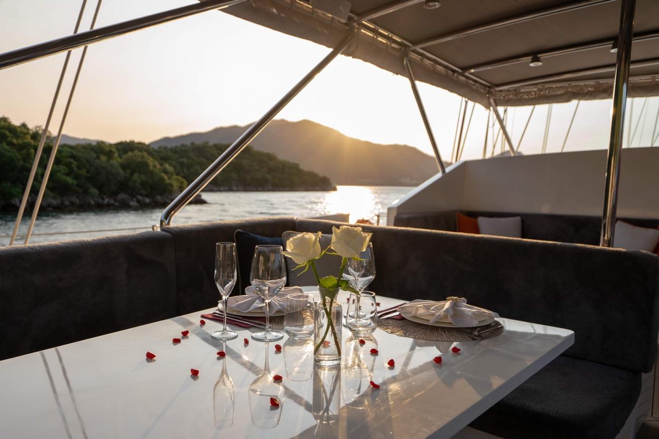 romantic dinner table with white roses, wine glasses and red rose petals at sunset