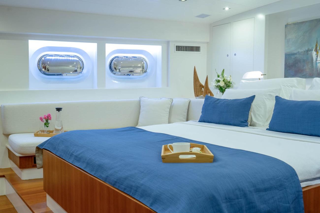 yacht guest cabin featuring double bed with blue bedding and two oval portholes