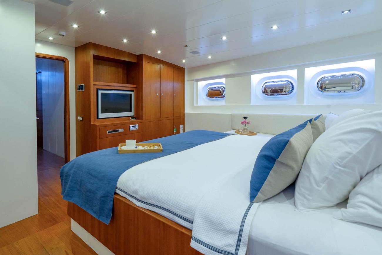 yacht cabin featuring double bed with blue runner, built-in entertainment center, and three oval portholes