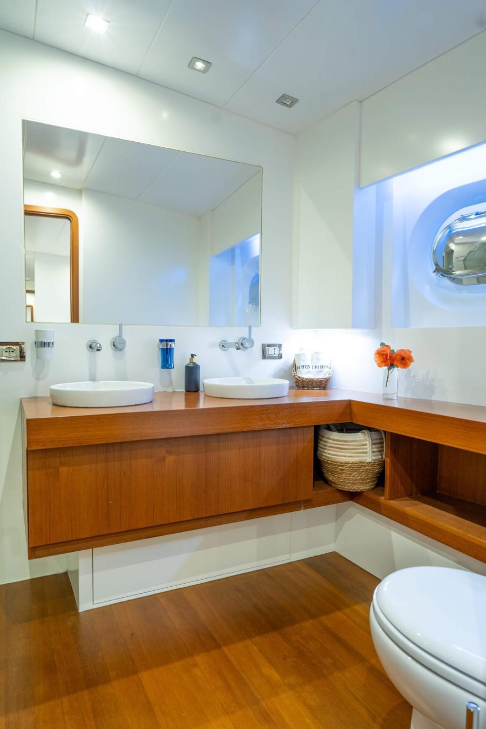 modern yacht bathroom featuring dual white vessel sinks on teak wood vanity with large mirror