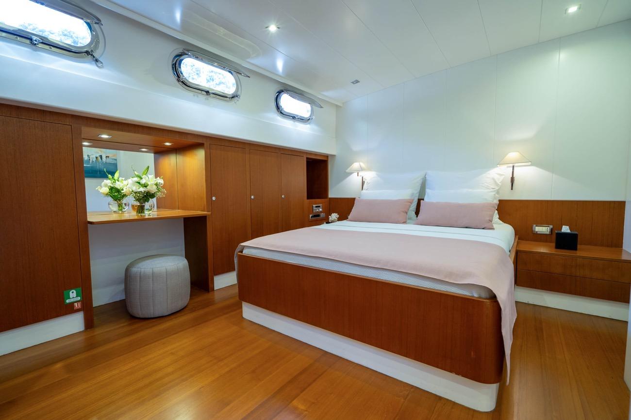 yacht cabin interior with double bed, wooden cabinetry, vanity desk and portholes