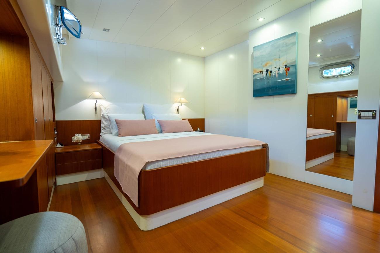 yacht cabin interior with double bed, wooden cabinetry, white walls and porthole window
