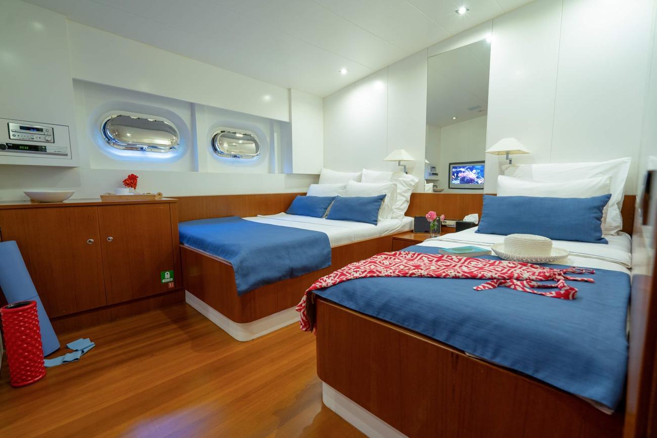 yacht twin cabin with two single beds, blue bedding, built-in storage and portholes