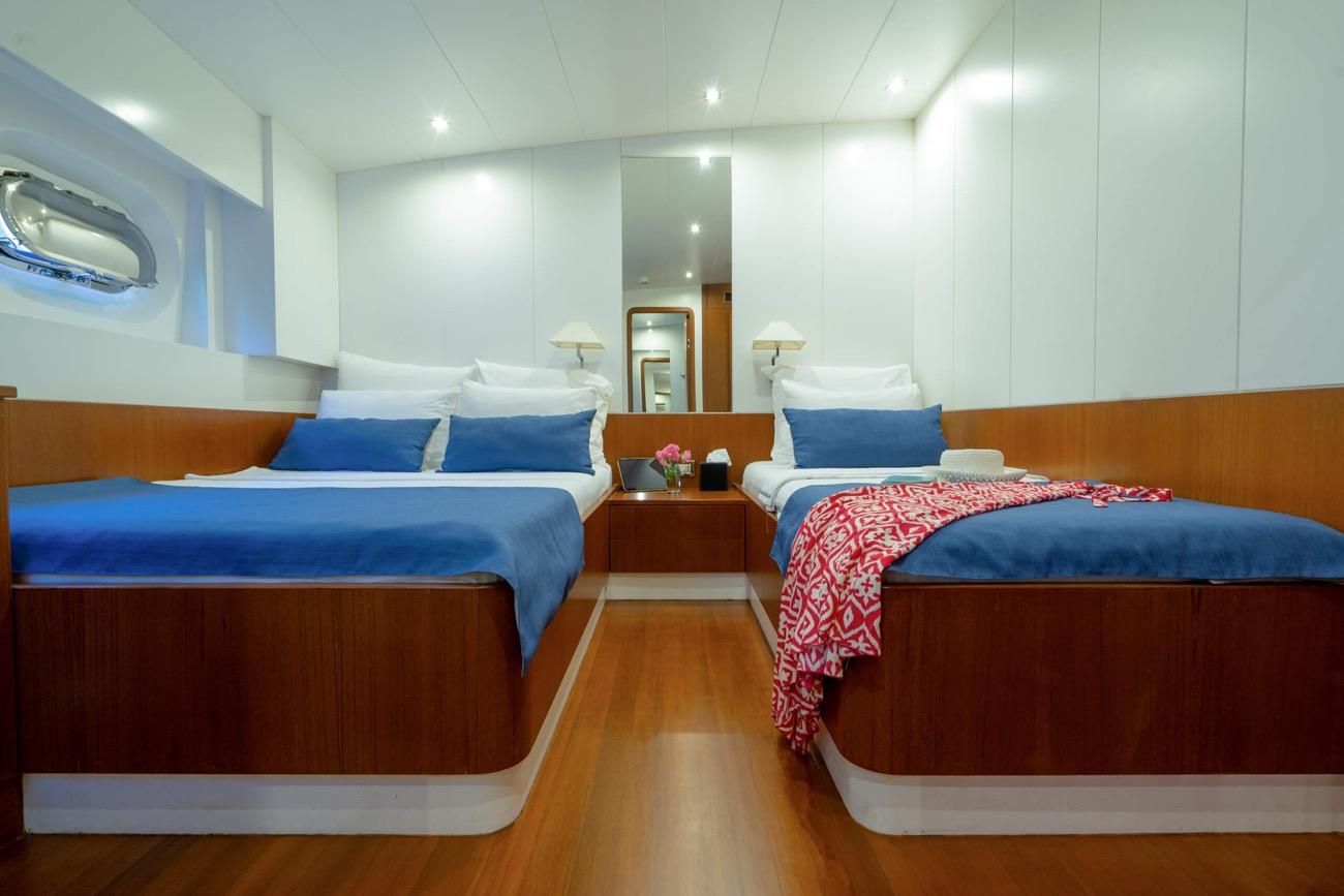 yacht twin cabin with two single beds, blue bedding, wooden paneling and white walls