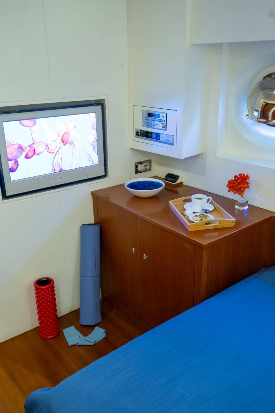 yacht cabin interior featuring blue bedding, wall-mounted TV, wooden storage unit and control panels