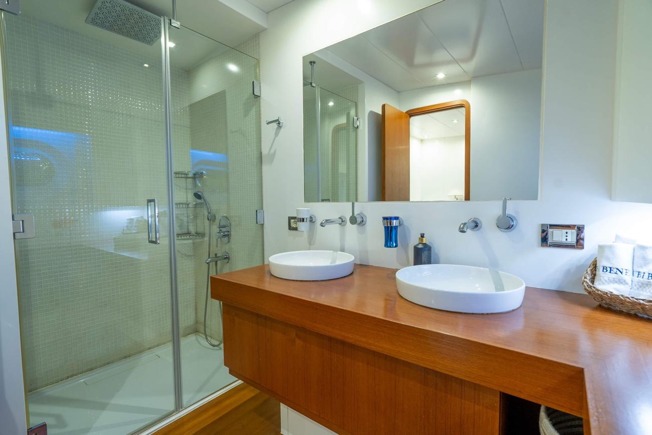 yacht bathroom featuring dual white vessel sinks on wood vanity with glass enclosed shower