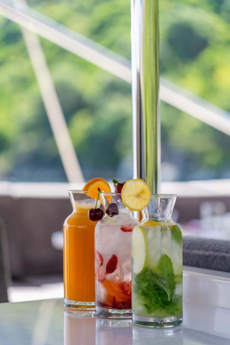 Three garnished cocktails with orange juice, berries and mint served on yacht table