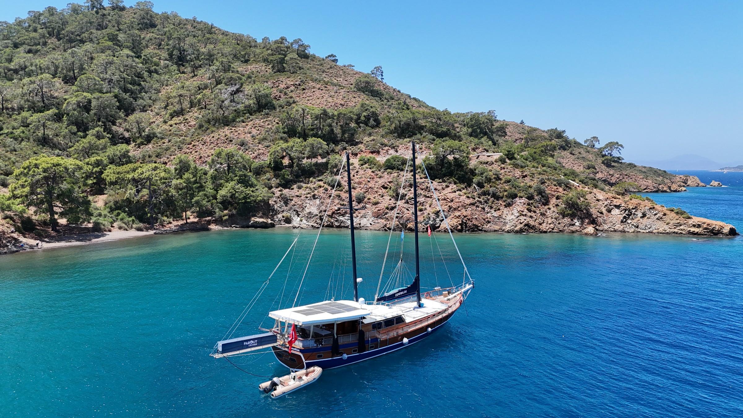 Aerial view of traditional wooden gulet anchored in crystal clear turquoise Mediterranean bay with tender alongside